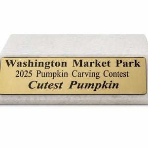 May include: A white marble award with a gold plaque. The plaque reads "Washington Market Park 2025 Pumpkin Carving Contest Cutest Pumpkin."
