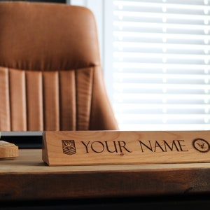 May include: A wooden desk nameplate with a bevelled edge. The nameplate has a carved design of a military insignia and the text "YOUR NAME".
