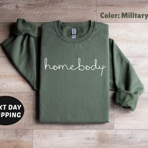 May include: A military green sweatshirt with the word "homebody" written in white script on the front.