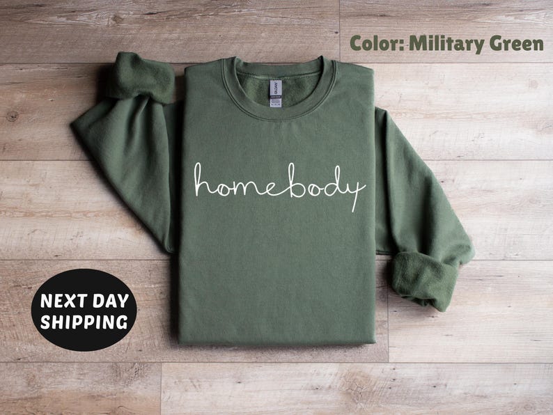 May include: A military green sweatshirt with the word "homebody" written in white script on the front.