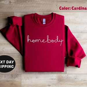 May include: Cardinal red sweatshirt with the text "homebody" in white script.