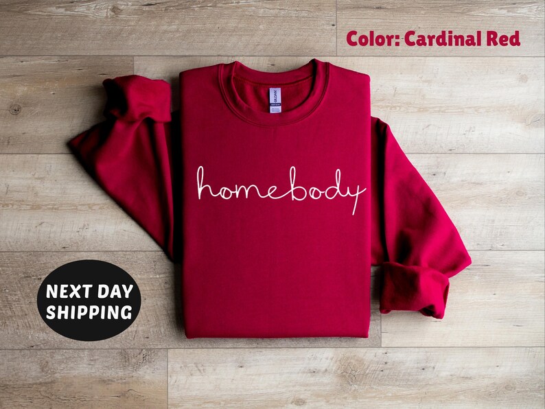 May include: Cardinal red sweatshirt with the text "homebody" in white script.