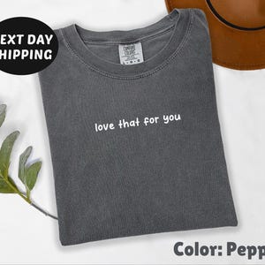 May include: A gray t-shirt with the text "love that for you" printed in white. The shirt is made of a soft, comfortable fabric.