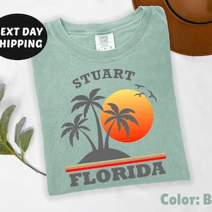 May include: A light green t-shirt with a graphic design of palm trees and a sunset. The text "Stuart Florida" is printed on the shirt.