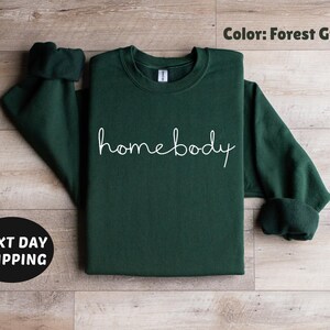 May include: Forest green sweatshirt with the text "homebody" in white lettering.