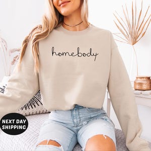 May include: A beige sweatshirt with the text "homebody" written in black cursive script.