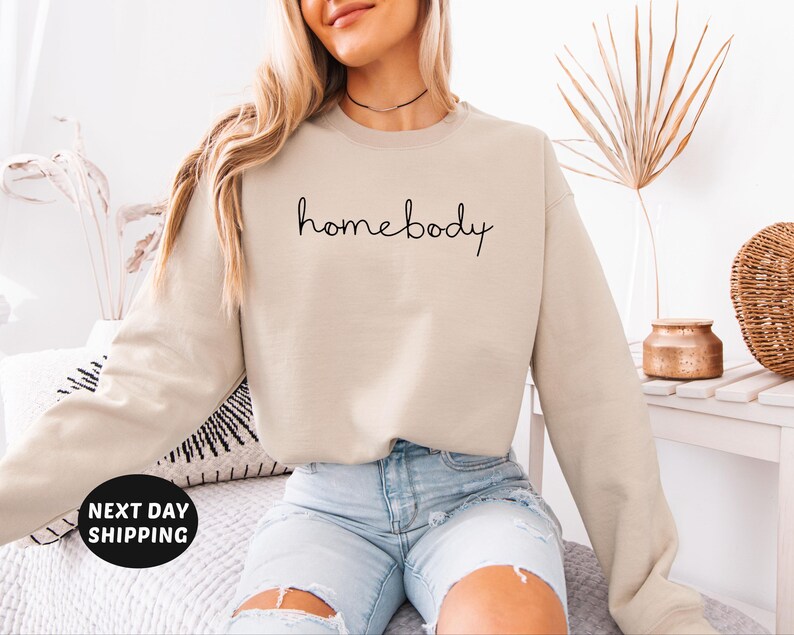 May include: A beige sweatshirt with the text "homebody" written in black cursive script.