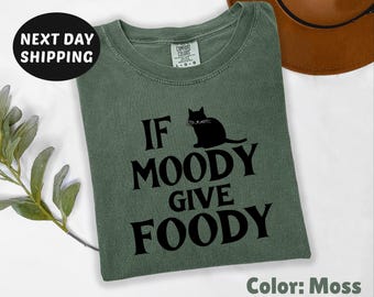 May include: A green t-shirt with the text "If Moody Give Foody" and a black cat silhouette. The text is in a bold, black font.