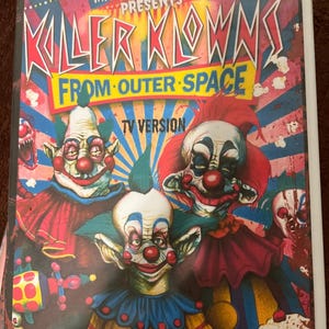May include: A VHS tape cover for "Killer Klowns From Outer Space" featuring menacing clown illustrations. The title is in large, stylized letters with the text "TV Version" at the bottom. The background has a circus-like design with red, blue, and yellow colors.