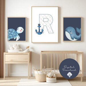 Può includere: Tre stampe incorniciate a tema nautico. Una presenta una tartaruga blu, un'altra una balena blu e la terza la lettera "R" con un'ancora. Le stampe sono in un ambiente di asilo nido con una culla e mobili in legno.