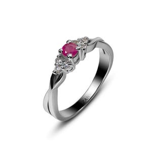Könnte beinhalten: Ein silberner Ring mit einem verdrehten Banddesign. Der Ring hat einen zentralen, runden, leuchtend roten Edelstein, flankiert von kleineren, klaren Edelsteinen. Der Ring ist vor einem weißen Hintergrund platziert.