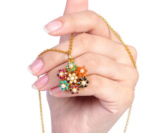 May include: A gold chain necklace with a multi-colored flower pendant. The pendant is made of gold and features a variety of gemstones, including red, orange, yellow, green, blue, and purple.