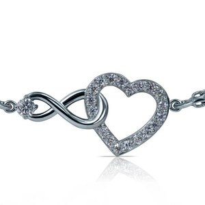 Può includere: Un braccialetto d'argento con un simbolo dell'infinito e un ciondolo a forma di cuore. Il cuore è incastonato con piccole pietre scintillanti. Il braccialetto ha un delicato design a catena e una piccola pietra rotonda sulla chiusura.