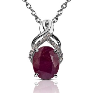 May include: A silver pendant necklace featuring an oval-cut, deep red ruby gemstone. The ruby is accented with small, sparkling clear stones and set in a decorative silver setting. The necklace hangs from a delicate silver chain.