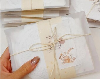 May include: Stacks of white paper packages tied with twine and adorned with decorative paper tags. Each package features a unique vintage-style illustration and a small, round sticker. The packages are wrapped in translucent paper.