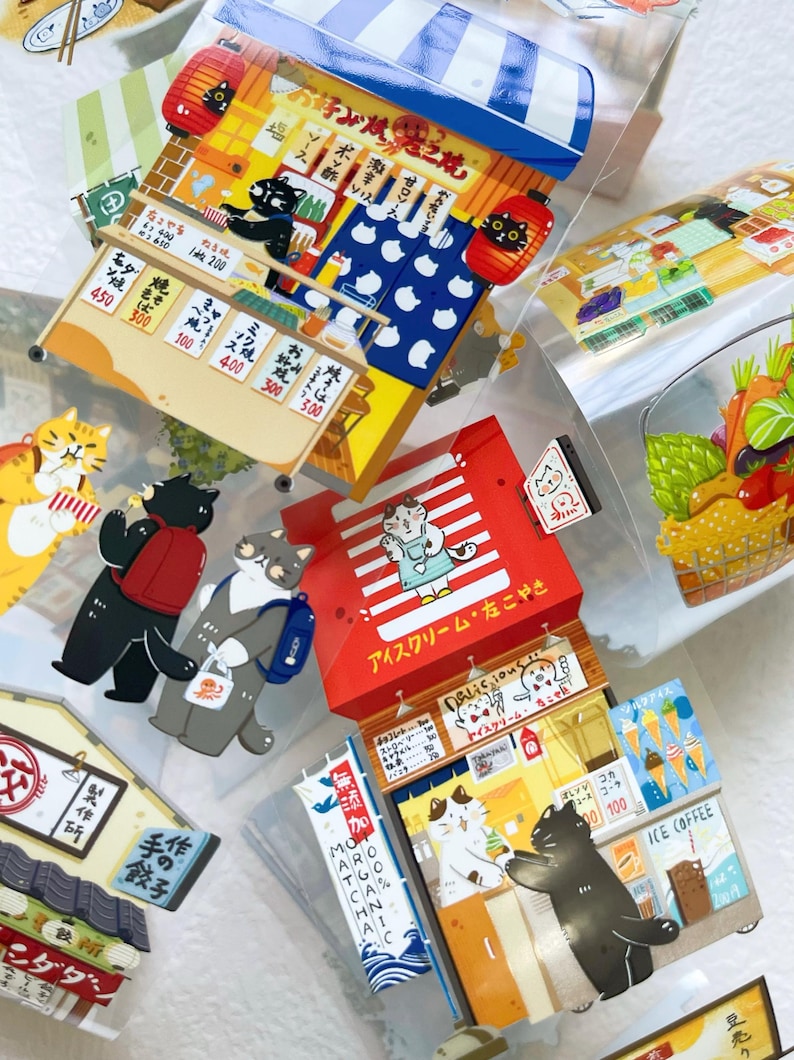 May include: A collection of colorful, illustrated stickers featuring cartoon cats in various settings. The stickers depict Japanese food stalls, ice cream shops, and other scenes with Japanese text and prices.