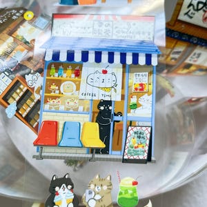 May include: A colorful sticker sheet featuring a cat-themed coffee shop scene. The shop has a blue awning, a sign that says "COFFEE TIME", and colorful drinks and pastries. There are also cat characters holding drinks and taking photos.