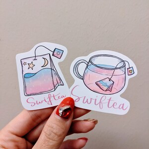 May include: Two stickers featuring Swifttea designs. One shows a tea bag with a moon and stars, the other a teacup with a tea bag inside. Both have a pink, blue, and purple gradient and the word "Swifttea" in pink script.