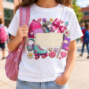 Könnte beinhalten: Ein weißes T-Shirt mit einem Grafikdruck, der einen pinken Rucksack, eine Discokugel, eine große pinke Schleife, einen türkisfarbenen Rollschuh, Kopfhörer, einen Stift, ein lila Notizbuch, einen Smiley-Anhänger und Blumen zeigt.