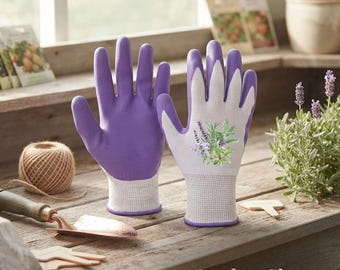 May include: A pair of gardening gloves featuring a solid purple palm and a white back with a printed lavender and herb graphic. The gloves have a textured grip on the palm and a white ribbed cuff. The text Garden Gloves is visible at the bottom.
