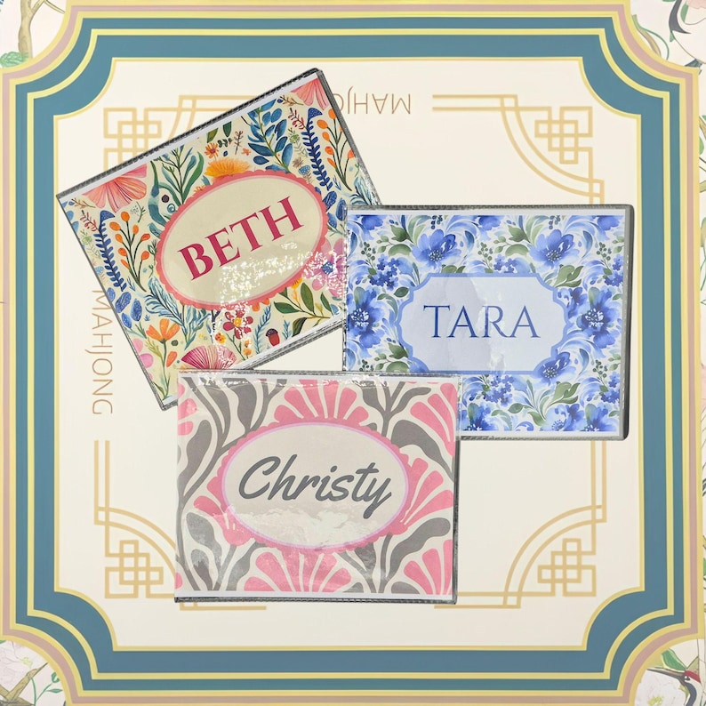 May include: Three rectangular personalised items in clear plastic packaging. One features a colourful floral pattern with the name BETH in red. Another has a blue floral design with the name TARA in blue. The third has a pink and grey pattern with the name Christy in grey.