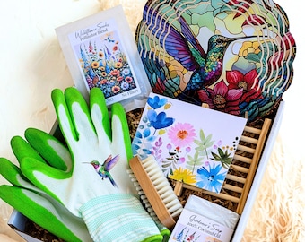 May include: A gift box containing a hummingbird wind spinner, a pair of light green and white gardening gloves with a hummingbird print, a packet of wildflower seeds, a floral greeting card, a wooden nail brush, and a bar of Gardener's Soap.