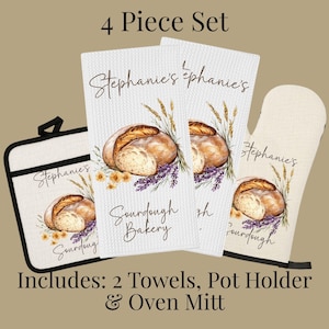 Op de afbeelding: Een 4-delige keukenset bestaande uit twee witte wafelstructuur theedoeken, een vierkante pannenlap en een ovenwant. Elk item is voorzien van een illustratie van zuurdesembrood, tarwearen en lavendel met de tekst Stephanie's Sourdough Bakery.