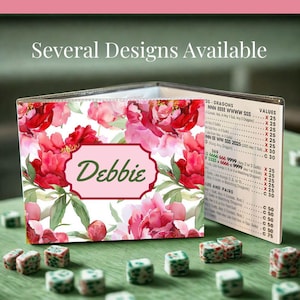 May include: A clear plastic Mahjong card sleeve featuring a floral pattern of pink peonies and green leaves. A central rectangular label displays the name Debbie in green script. The sleeve holds a printed Mahjong score card with visible text.