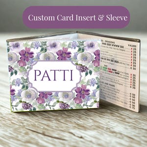 Op de afbeelding: Een aangepaste kaartinzet en hoes met een bloemenpatroon in tinten paars, lavendel en groen. De voorzijde toont de naam PATTI in een wit rechthoekig kader. De zijkant toont een bedrukte Mah Jongg-scorekaart met bijbehorende puntenwaarden.