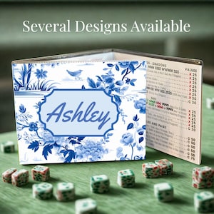 May include: A folding game score card featuring a blue and white floral pattern with a bird illustration and the name Ashley in a central light blue frame. The interior panel displays a printed list of game rules and point values for Mahjong.