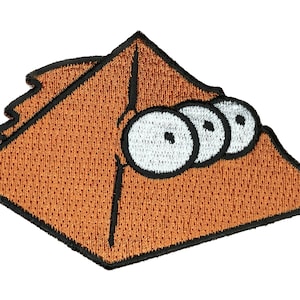 May include: A brown felt patch with a triangular shape and three white eyes with black pupils. The patch has a black outline.