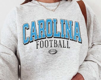 May include: Gray sweatshirt with blue text that reads "CAROLINA FOOTBALL" and a small football graphic.