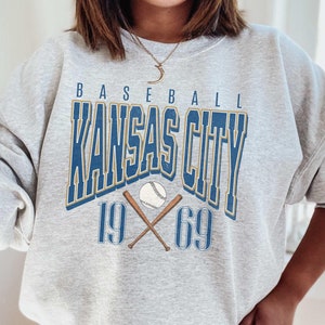 Peut inclure: Sweat-shirt gris avec un motif bleu et or qui dit "Baseball Kansas City 19 69" avec un ballon de baseball et des chauves-souris crois&eacute;es.