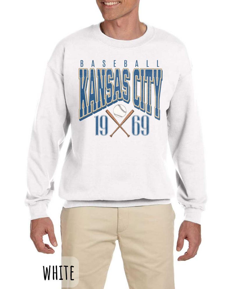 Peut inclure: Sweat-shirt blanc avec un motif bleu et or qui dit "Baseball Kansas City 19 69" avec un ballon de baseball et des chauves-souris crois&eacute;es.