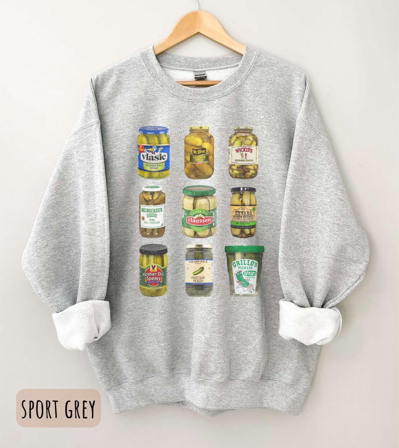 Op de afbeelding: Sportgrijs sweatshirt met een afbeelding van augurkenpotten. De potten zijn gevuld met augurken en hebben verschillende merknamen. De sweatshirt heeft een ronde hals en lange mouwen met witte manchetten. De tekst "SPORT GREY" staat onderaan.