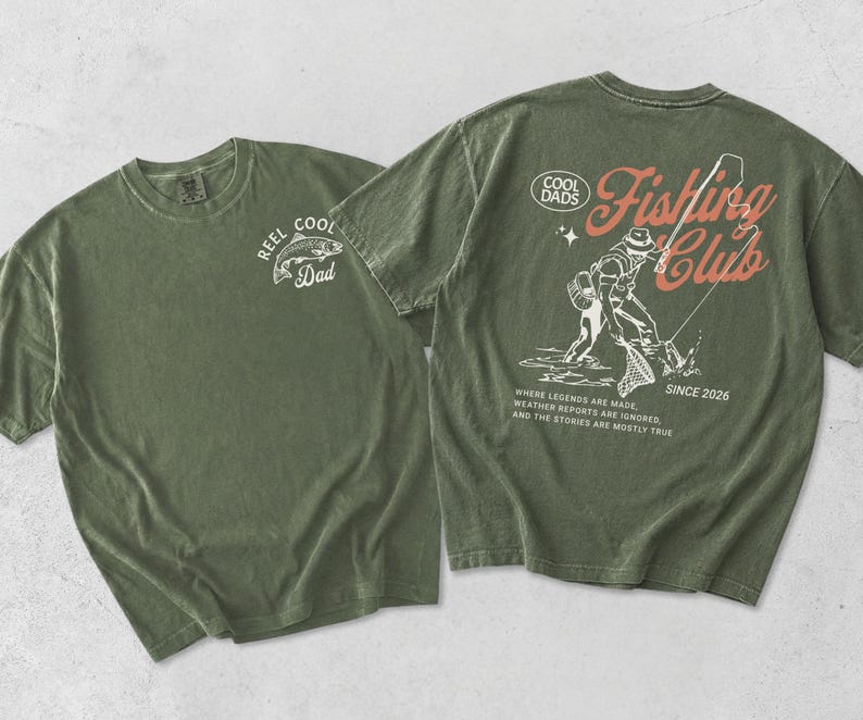 May include: Two olive green t-shirts. One has a white fish graphic and the text "REEL COOL Dad". The other features a fishing scene graphic with the text "COOL DADS Fishing Club SINCE 2026".