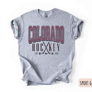 May include: A grey t-shirt with a burgundy graphic that says "Colorado Hockey Est. 1979" with a pair of crossed hockey sticks.