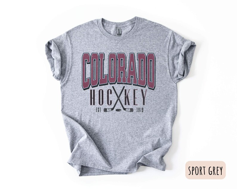 May include: A grey t-shirt with a burgundy graphic that says "Colorado Hockey Est. 1979" with a pair of crossed hockey sticks.
