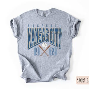 Peut inclure: Un t-shirt gris avec un design graphique de style vintage repr&eacute;sentant le texte "Baseball Kansas City 1969" avec un ballon de baseball et des chauves-souris crois&eacute;es.