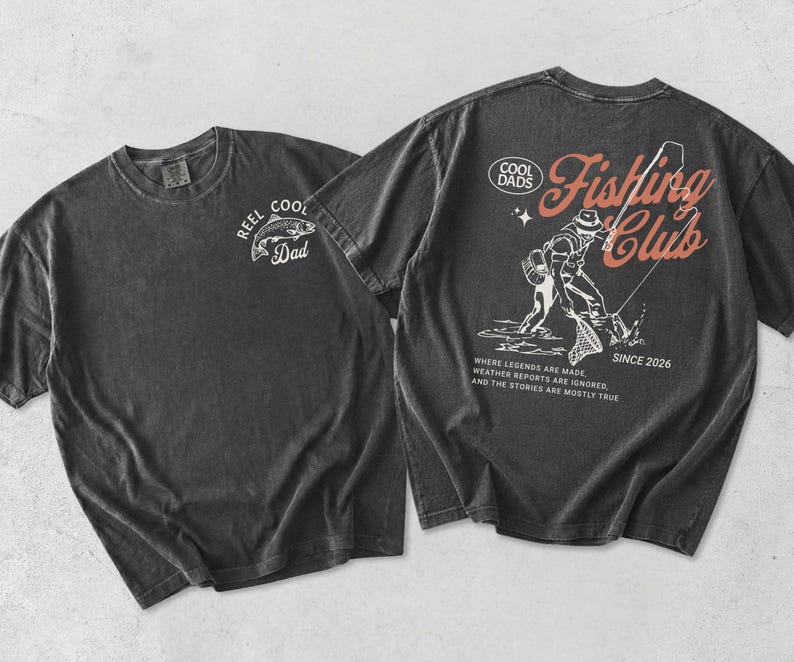 May include: Two charcoal grey t-shirts. One has a white graphic of a fish and the text "REEL COOL Dad". The other features a fishing-themed design with the words "Fishing Club" and "Since 2026". The text "Where legends are made, weather reports are ignored, and the stories are mostly true" is also included.