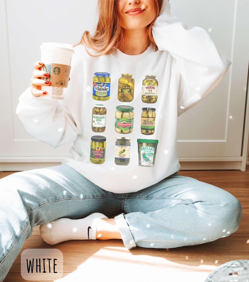 Op de afbeelding: Witte sweatshirt met een kleurrijke afbeelding van verschillende augurkenpotten. De potten zijn gevuld met augurken en hebben verschillende merklabels. Het woord "WHITE" staat onderaan de afbeelding.