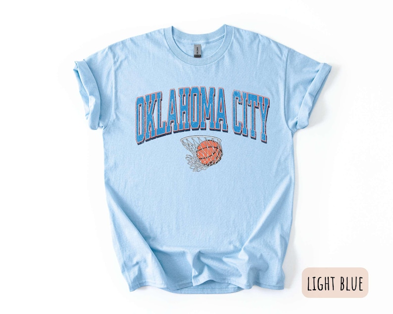 May include: Light blue t-shirt with the text "OKLAHOMA CITY" in blue and red lettering. A basketball is shown going through a hoop.