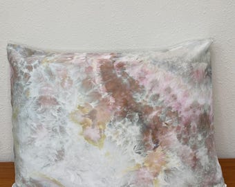 Puede incluir: Una funda de almohada rectangular con un patrón de teñido anudado en tonos mezclados de rosa suave, marrón apagado, amarillo pálido y blanco. La tela muestra una estética marmolada y nublada con transiciones de color orgánicas y fluidas.