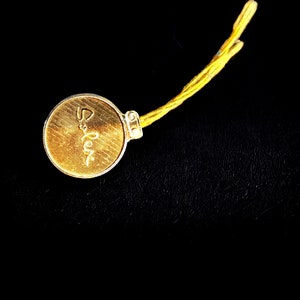 May include: A gold-coloured metal tag with the word "Salex" inscribed on it. The tag is attached to a yellow string.