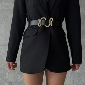 May include: A black blazer with a snake-shaped belt buckle. The blazer has a notched lapel and long sleeves.