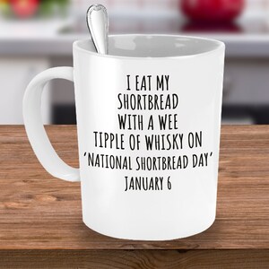 Puede incluir: Taza de cerámica blanca con texto negro que dice "Me como mi shortbread con un pequeño sorbo de whisky en el 'Día Nacional del Shortbread' 6 de enero".