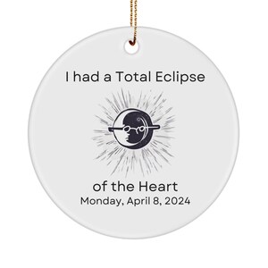 May include: White round ceramic ornament with a black and white illustration of a sun and moon with a pair of glasses. The text reads "I had a Total Eclipse of the Heart Monday, April 8, 2024".