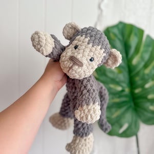 Peut inclure: Une peluche singe au crochet faite &agrave; la main, dans des tons de gris et de beige. Le singe a un aspect textur&eacute; et doux avec un visage d&eacute;taill&eacute;, comprenant de petits yeux noirs et un museau beige. Les bras et les jambes sont tendus.