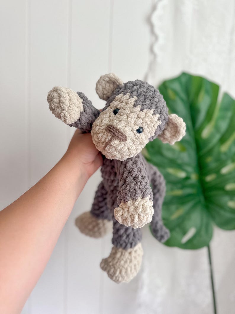 Peut inclure: Une peluche singe au crochet faite &agrave; la main, dans des tons de gris et de beige. Le singe a un aspect textur&eacute; et doux avec un visage d&eacute;taill&eacute;, comprenant de petits yeux noirs et un museau beige. Les bras et les jambes sont tendus.