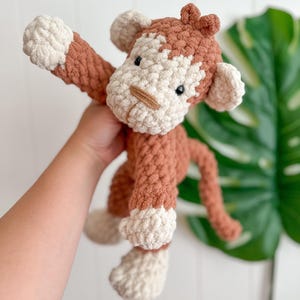 Peut inclure: Une peluche singe au crochet faite &agrave; la main, dans des tons de marron et de cr&egrave;me. Le singe a un aspect textur&eacute; et doux avec une longue queue et des bras tendus. Le visage du jouet pr&eacute;sente de petits yeux noirs et un nez beige.